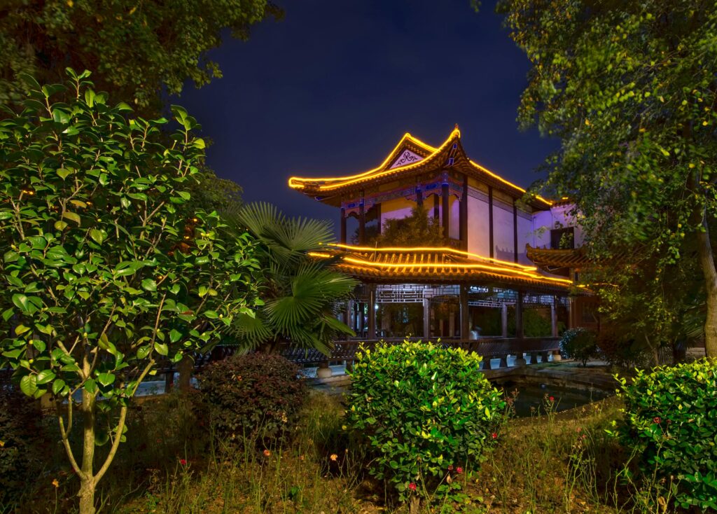 Illuminated Chinese pavilion at night amidst lush garden in Huangshi Shi, Hubei.